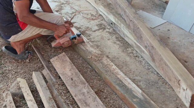 Stock video showing an electric planer tool actively shaving wood material, generating fine sawdust shavings along the timber board.