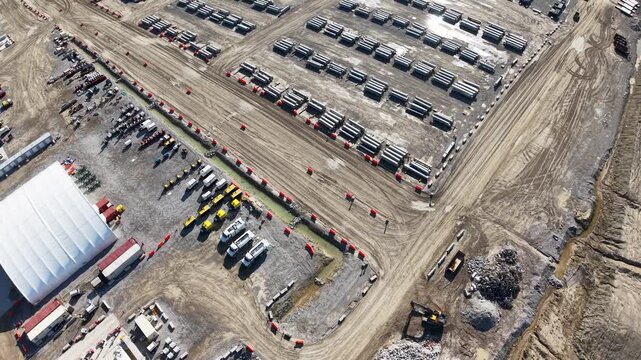 Top down drone view of organized material rows beside a warehouse and intersecting quarry roads