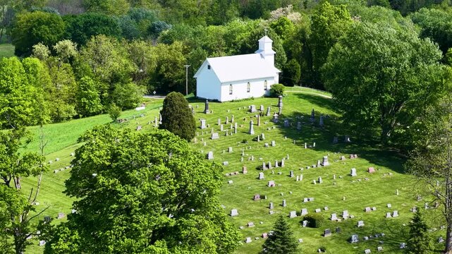 Aerial view of a white country church overlooking neat orchard rows within lush wooded countryside