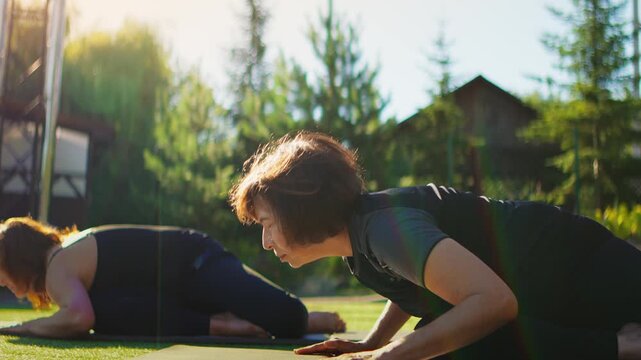 Elderly women practicing slow motion Pilates stretches outdoors on yoga mats, focusing on gentle flexibility, balance, and mindful movement in a peaceful garden setting