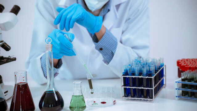 Close up of scientist hands using pipette dropping chemical liquid into test tube in laboratory.