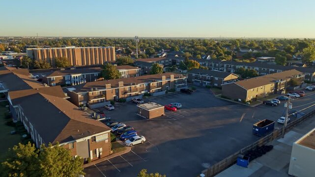 Sunset aerial view of a neighborhood with multifamily housing complexes, commercial buildings, and tree-lined streets.