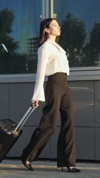 Beautiful young business woman walking on a city street with her luggage during a business trip, a confident female traveler arriving at her destination after a flight