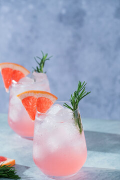 Close-up of a refreshing pink grapefruit cocktail with ice, fresh rosemary, and a juicy grapefruit wedge garnish.Vibrant macro food photography, restaurant menus, cocktail bars, healthy beverages