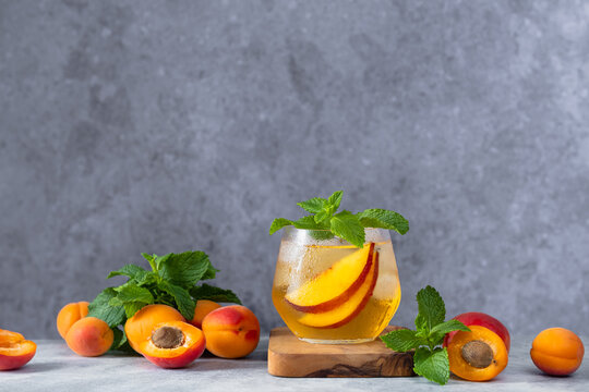 Refreshing summer apricot and nectarine cocktail served over ice with fresh mint leaves in a modern glass. The drink is garnished with juicy stone fruit slices and surrounded by ripe apricots