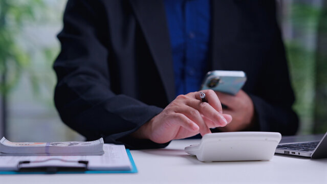 Professional accountant holding mobile phone calculates business expenses, tax payments, typing numbers, managing cash money bills, planning corporate investment strategies.