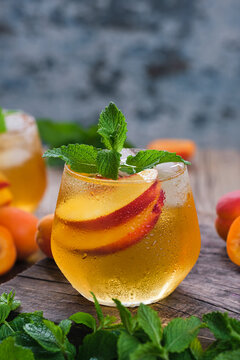 Cold summer beverage with sliced fresh nectarines, mint leaves, and ice in a condensed glass, garnished with fresh mint and fruit on a textured tabletop.