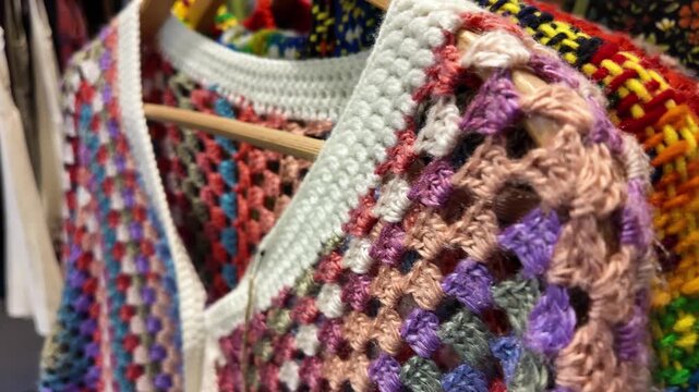 Colorful handcrafted crochet sweaters hanging on wooden hangers, showcasing intricate patterns and textures, dynamic video footage