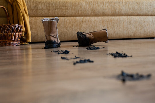 burnt ugg boots on living room floor with debris and couch in background. distressed home decor scene with brown and black tones and wooden floor. repair and damage repair concept.