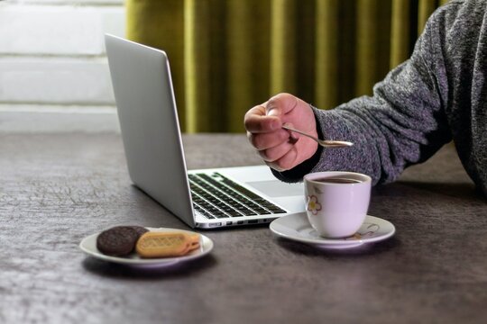 Person stirring a cup of hot chocolate with a spoon while working on a laptop at home