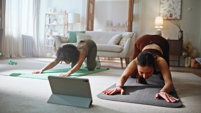 Two women doing yoga home following online tutorial tablet. Cobra pose workout.