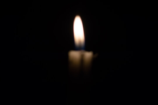 glowing candle flame shining softly with warm golden light against a complete dark pitch-black background, creating a peaceful and serene ambiance