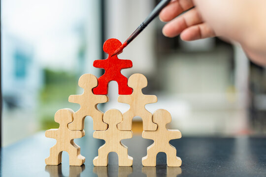 Leadership, recruitment and standing out from the crowd concept. Painting top wooden figure red. Ideal for human resources, career promotion, talent selection, and business management.