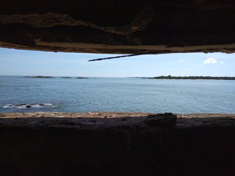 Looking through a concrete bunker slit at the sparkling blue ocean horizon