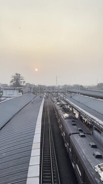 Vertical video showing sunset above a railway station with commuter trains and parallel tracks, representing urban transportation and daily travel.