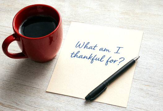 Handwritten note with pen and red coffee cup on wooden table expressing gratitude reflection