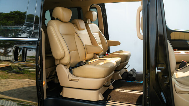 Interior of a premium van featuring tan leather captain seats with armrests and headrests, arranged in spacious rows. 