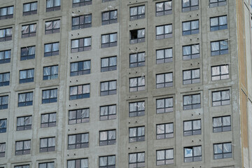Fototapeta premium Building under construction in an urban area with several windows and unfinished spaces present on the facade during daylight hours