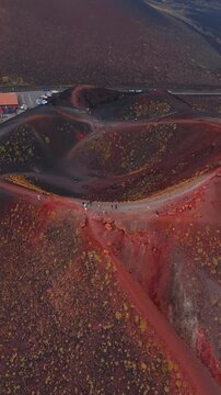 Hikers cross a path between ocre craters on Etna, vertical drone tilts down.