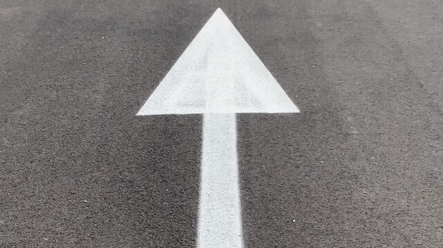 White arrow painted on asphalt road pointing forward. Concept of future growth, personal development motivation and business progression.