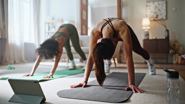 Women following online yoga class home. Fitness pair stretching pose tablet.