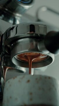 4K Pouring coffee stream from professional machine in cup. Barista man making double espresso, using filter holder. Flowing fresh ground coffee. Drinking roasted black coffee in the morning.