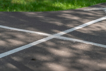 Obraz premium White painted lane markings crossing on textured asphalt road with dappled sunlight, soft tree shadows, shallow focus, urban surface detail, traffic safety context