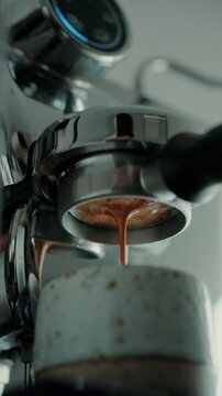 4K Pouring coffee stream from professional machine in cup. Barista man making double espresso, using filter holder. Flowing fresh ground coffee. Drinking roasted black coffee in the morning.