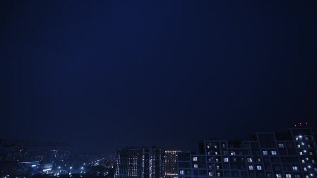Timelapse of dark clouds moving above illuminated apartment buildings in an urban residential district at night