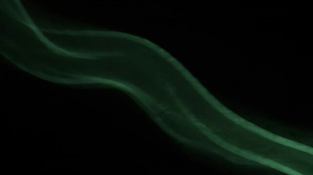 Abstract green smoke flowing across black background, ethereal light waves forming soft motion curves in dark space, mysterious vapor texture for artistic design visuals.