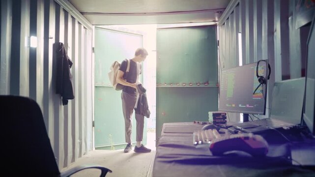 Man entering his secret hideout in an industrial container and starting to work on a computer