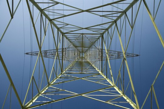 Looking up at high voltage electricity pylon steel structure against blue sky with electricity transmission electrical infrastructure structural industrial technology construction engineering