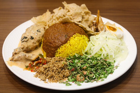 Nasi Kerabu featuring yellow turmeric rice topped with rich gravy, served with creamy chicken, shredded fresh ulam herbs, coconut floss, salted egg, and fish crackers.