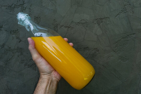 man hand holding orange juice bottle on dark black concrete cement wall, banner advertisement 