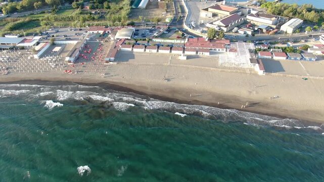 Miseno Beach Marine Resort Sweeping Across Sandy Tideline Umbrellas and Over Emerald Sea Waves. Beautiful Italian Coastline Panorama Hidden Behind Historic Waterfront Architecture. Drone Shot