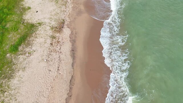 Aerial video shows waves crashing onto the sandy beach.