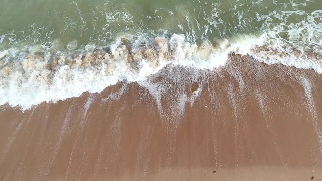 Aerial video shows waves crashing onto the sandy beach.