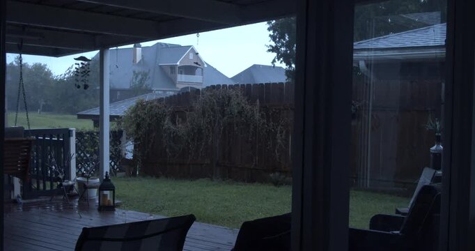 Cinematic rainy backyard patio viewed through window with suburban houses and wet deck during a peaceful stormy evening. Louisiana.