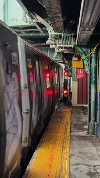 Subway train departs elevated outdoor platform with wet ground and signal lights visible