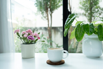 Coffee cup and pink carnation flowers and philodendron plant on white table © paladin1212