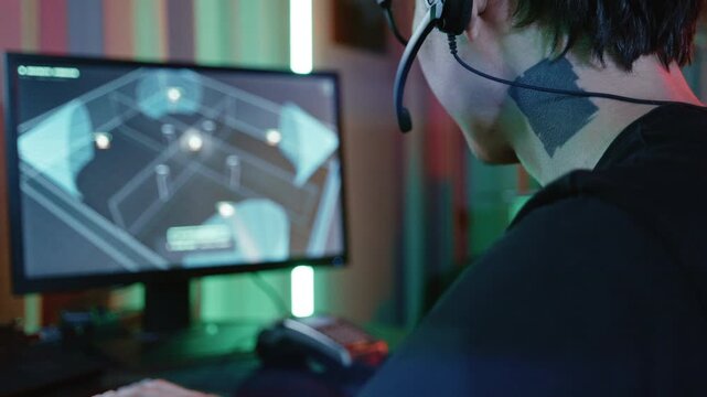 Young man with headset hacking into a building's cctv camera system on his computer in a dark room