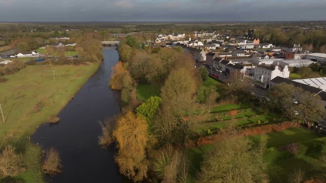Cinematic aerial drone shot of the River Barrow and Monasterevin town under a grey sky, featuring lush green banks and traditional Irish architecture.