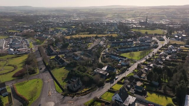 A cinematic aerial shot showcasing the authentic suburban landscape and green outskirts of Letterkenny, Donegal, Ireland during a bright afternoon.