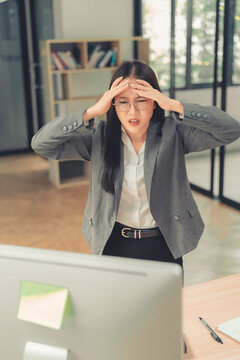 Stressed Asian businesswoman holding hand on forehead looking at computer screen with worried expression.