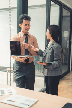 Two Asian business colleagues discussing work project on digital tablet in office.