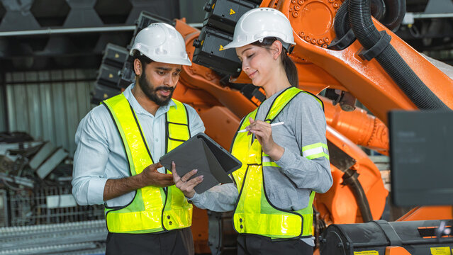 Engineering professionals reviewing maintenance documents and discussing equipment reliability beside an industrial robotic arm.