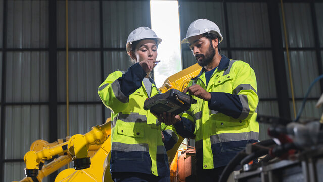 Two engineers discussing industrial robot performance and reviewing inspection information during a maintenance evaluation inside an automated factory.