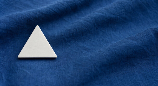 Single white equilateral triangle object on deep blue linen, calm still life for editorial concept