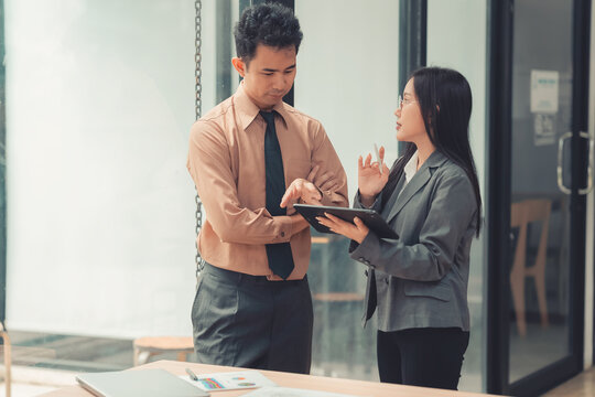 Two Asian business colleagues discussing work project on digital tablet in office.
