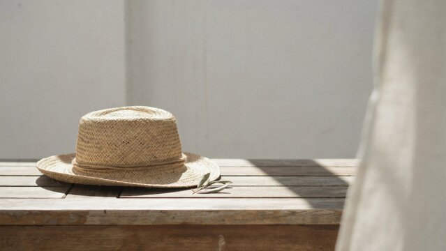Straw sun hat resting on wooden table in soft natural light with sheer curtain backdrop